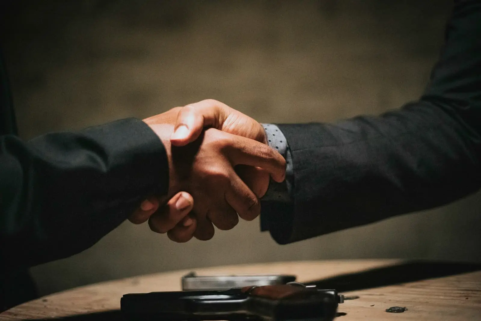 Two people shaking hands over a wooden table in a meeting