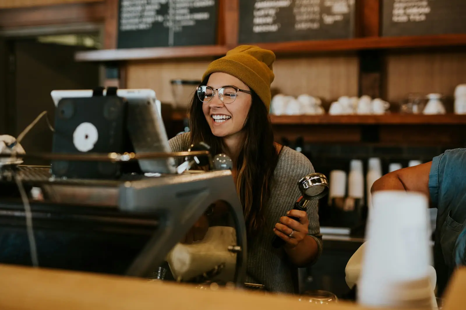 Woman holding a coffee portafilter behind the counter of a coffee shop