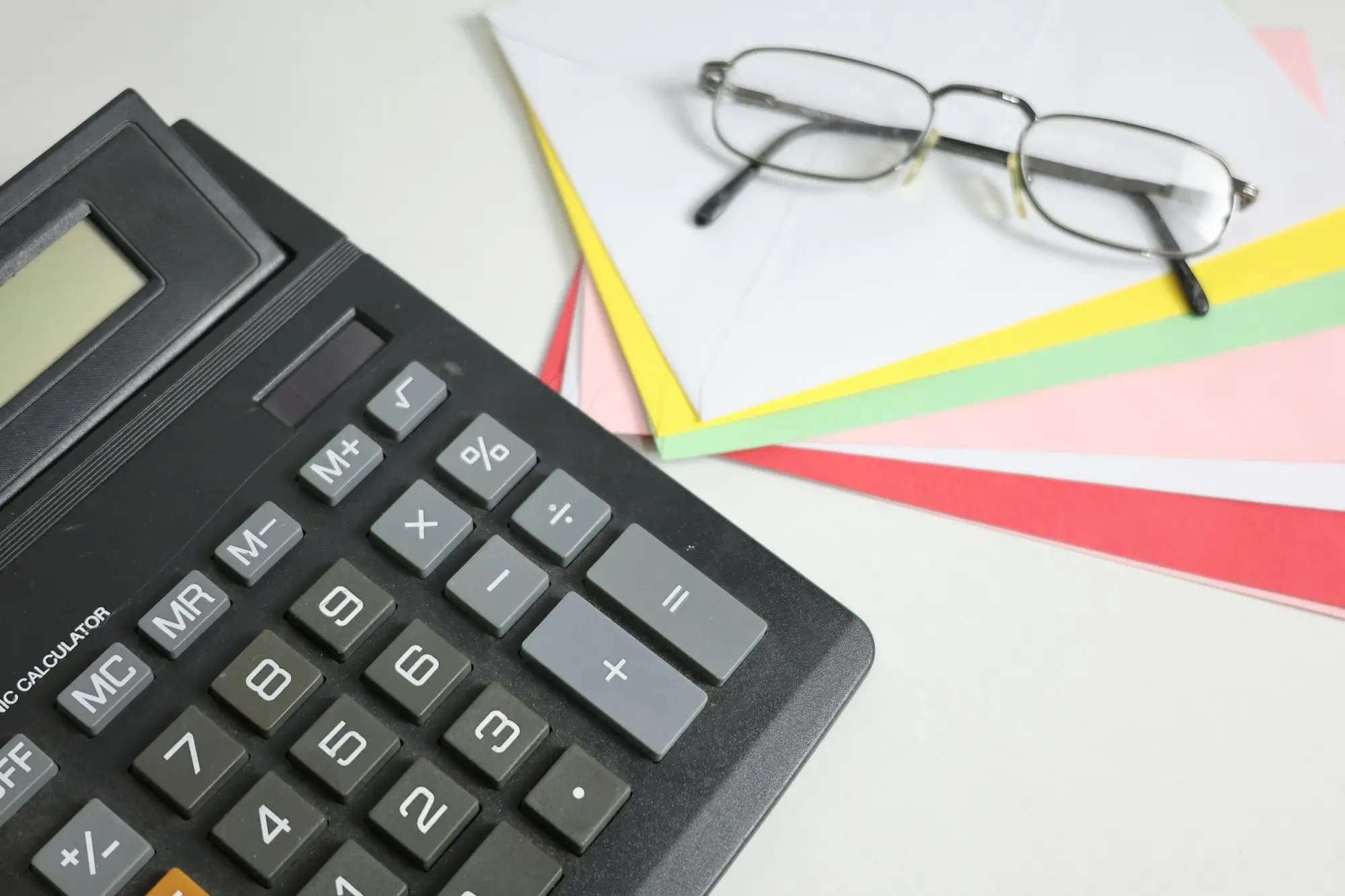 Desk calculator beside reading glasses and a stack of coloured papers, ready to work out a debt-to-income ratio