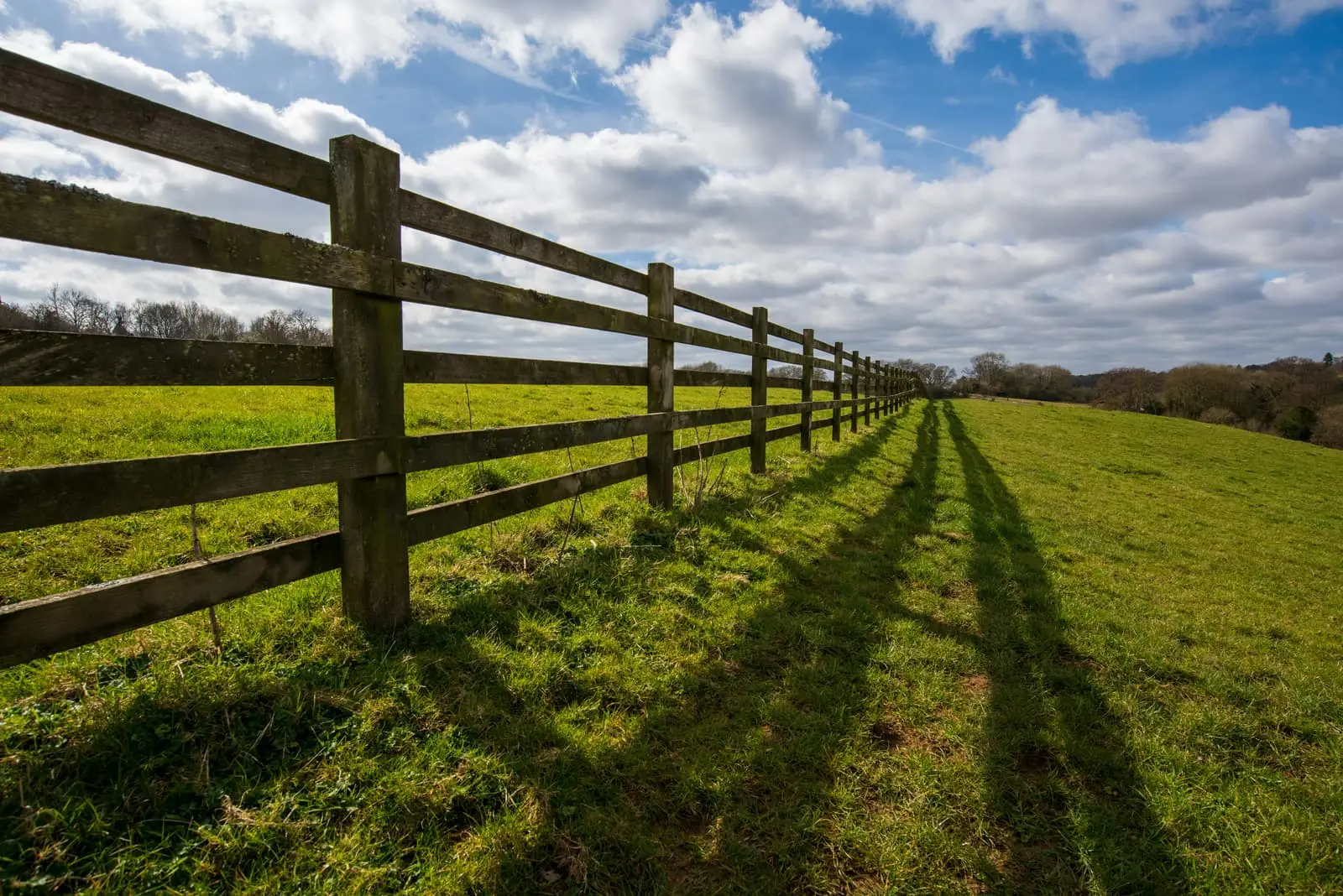 Long post and rail fence running across a grassy field under blue sky