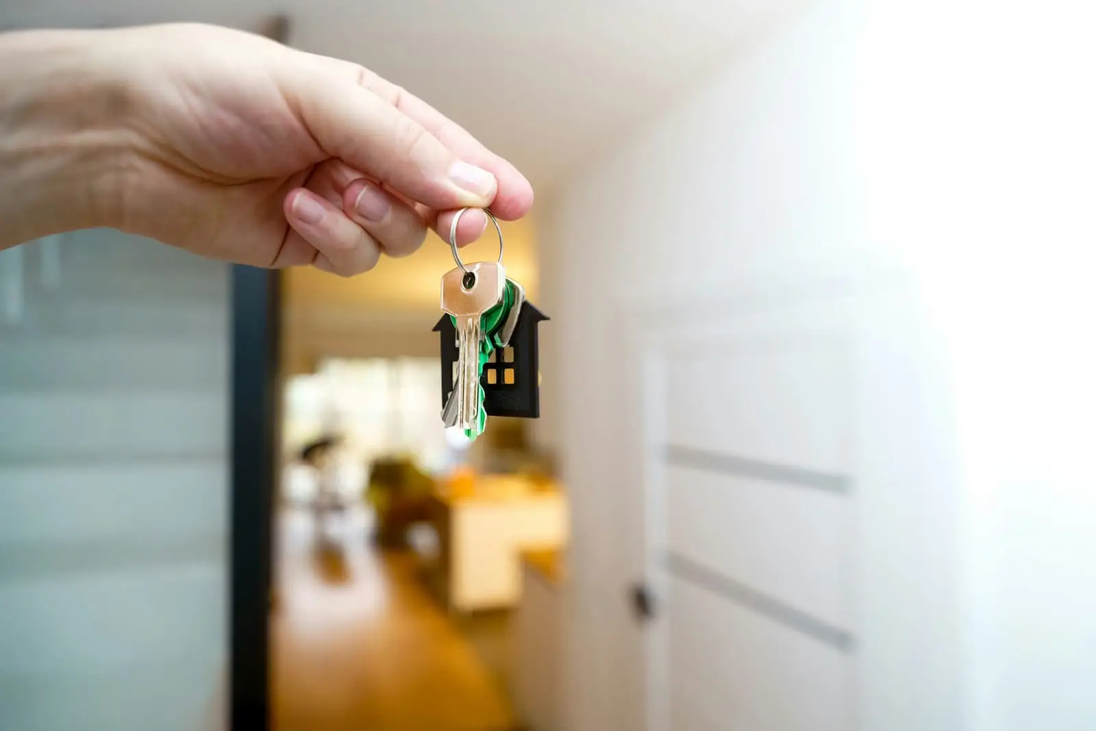 Hand holding house keys in front of a home entrance