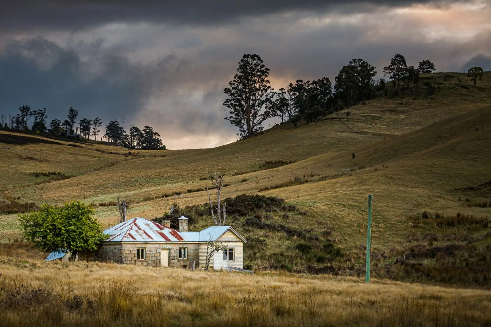 White and brown house on a green grass field under grey clouds