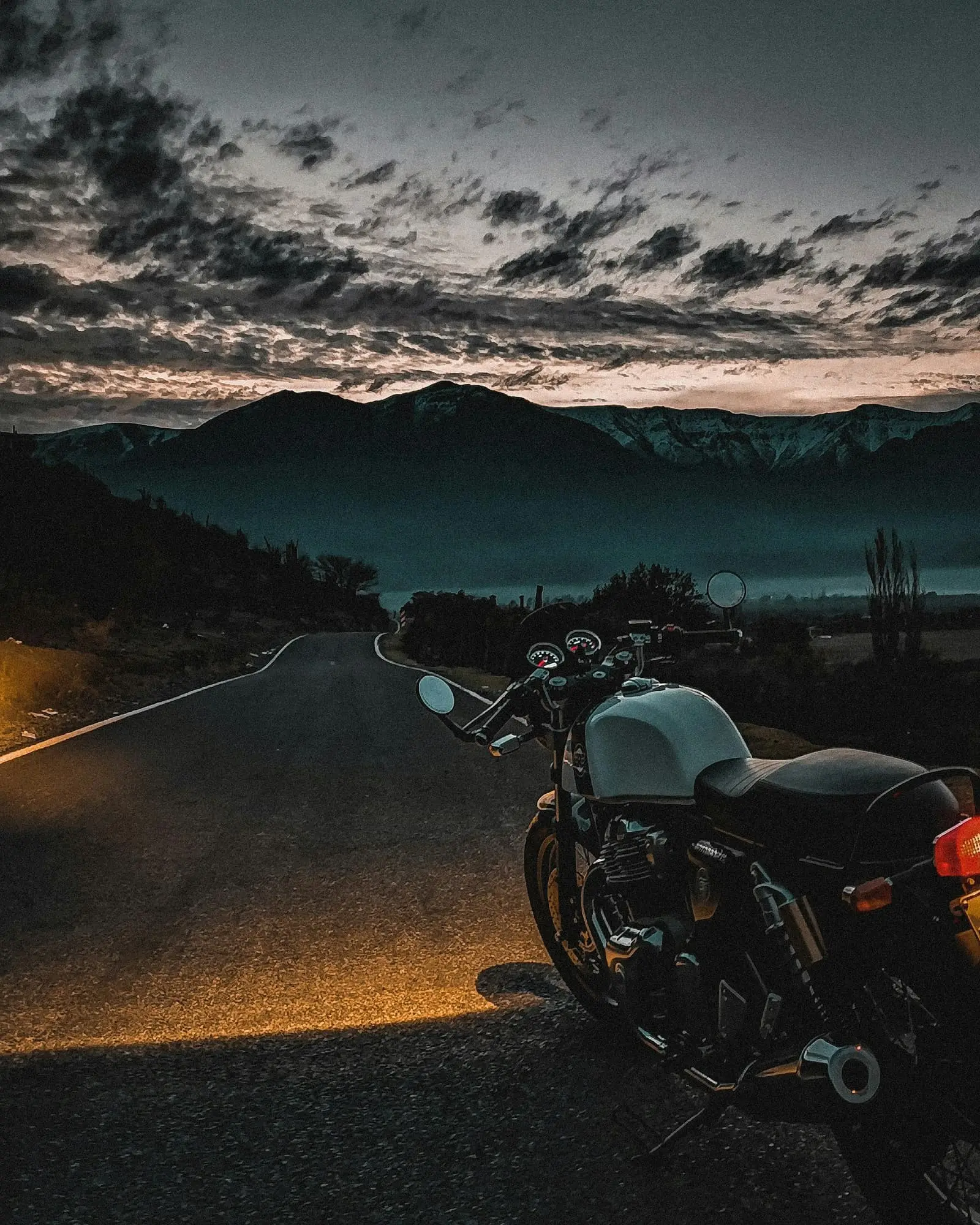 Motorcycle parked on an open road leading toward dark mountains under cloud