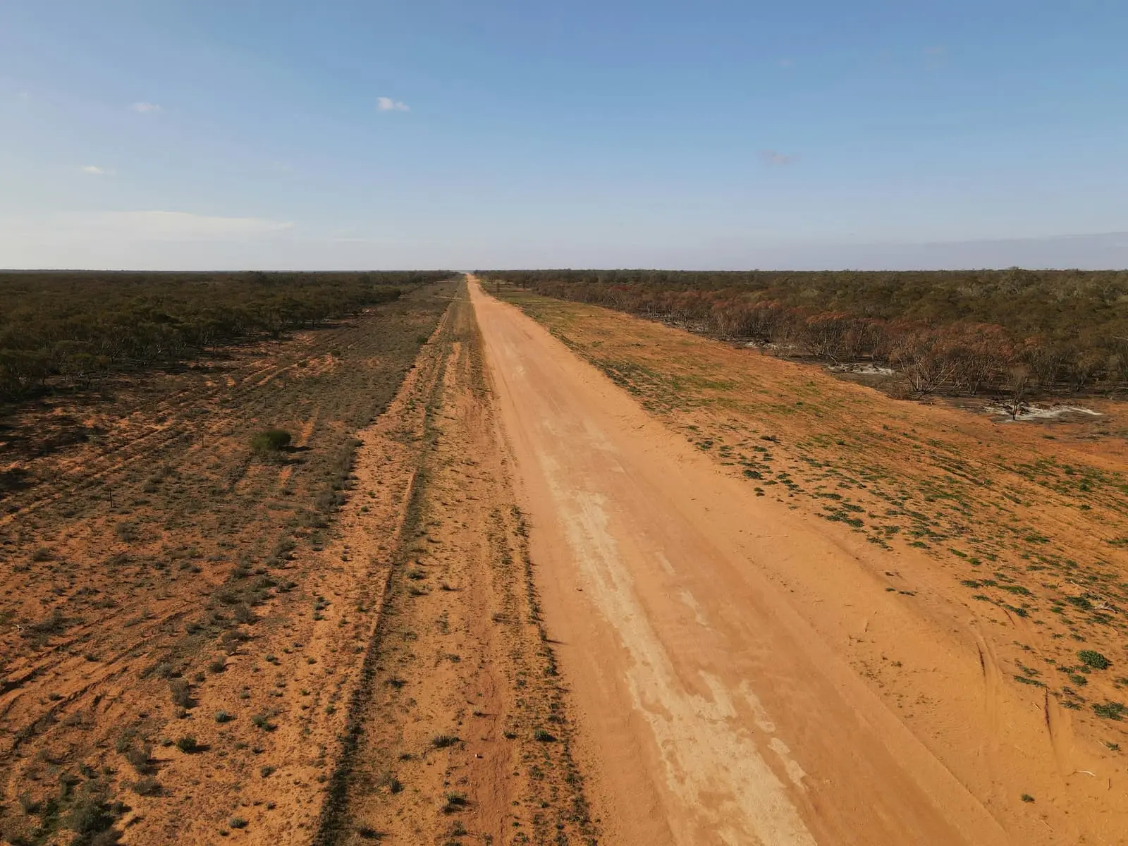 Brown dirt road stretching through open country under a blue sky