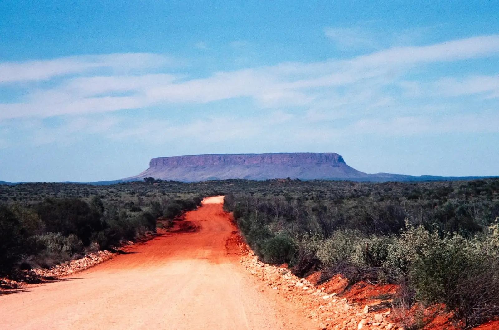 Dusty red road through scrubland towards a distant mesa in the outback