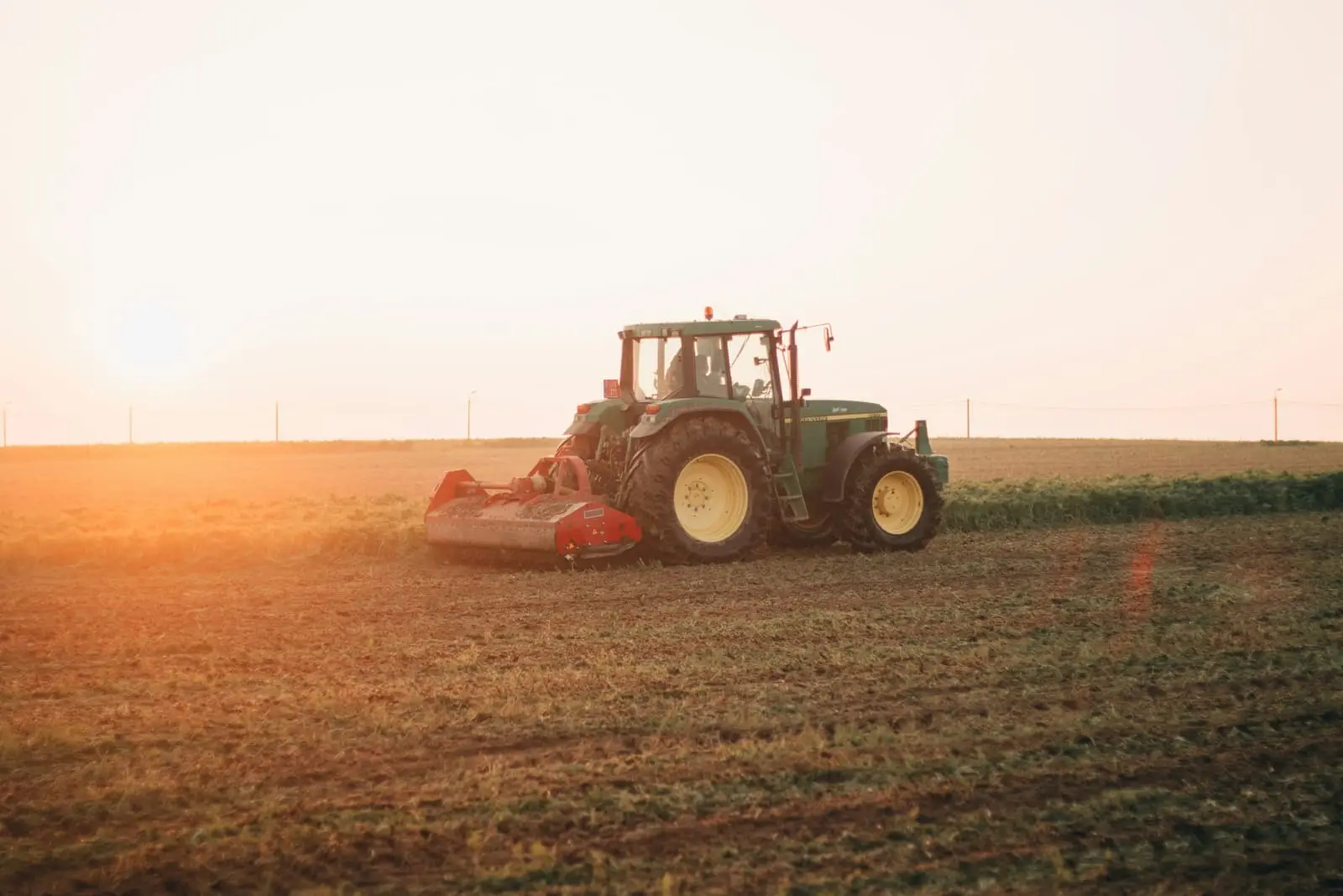 Red tractor working a brown field in the daytime