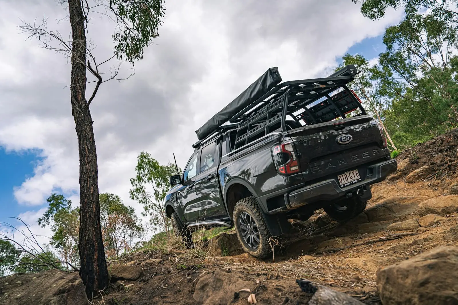 Black pickup ute driving up a rocky bush track in the hills